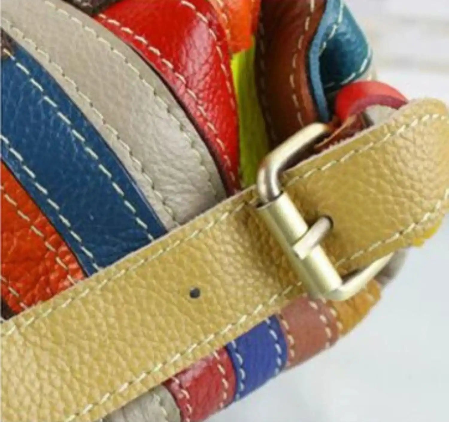 Detail of a colorful leather bag with a beige leather handle, highlighting the stitching and metal clasp.