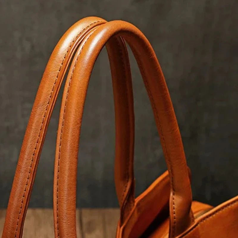 Detail of the handles of a brown leather bag, highlighting the texture and exquisite finish.