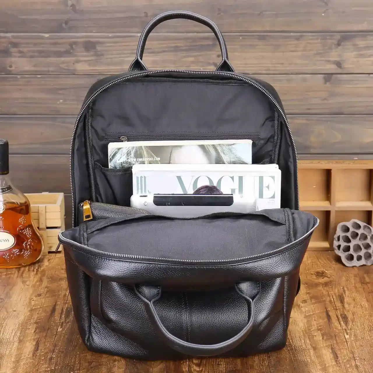 A black leather backpack showcasing its spacious interior with books and a tablet.