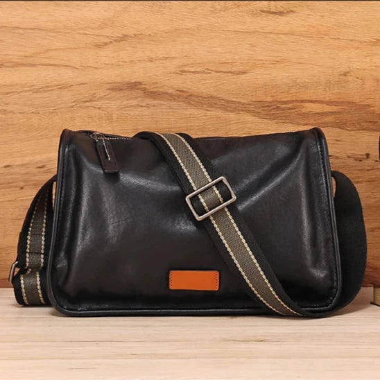 Black leather messenger bag with adjustable striped fabric strap, front view.