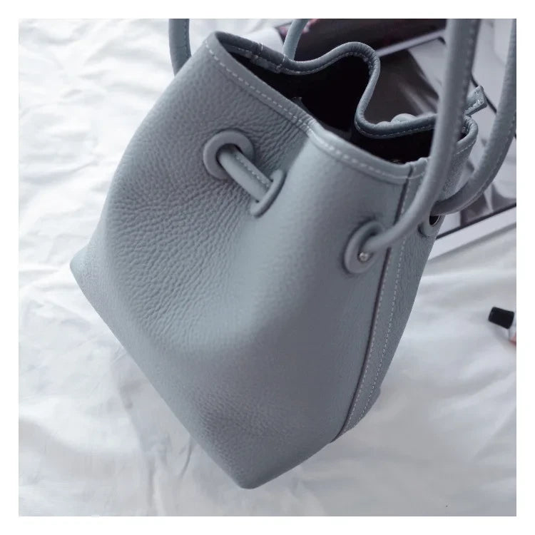 A stylish light blue leather bucket bag with a textured surface and adjustable straps.