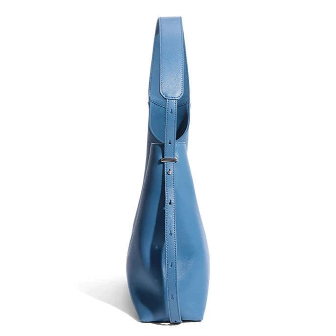 Elegant blue leather bag with a modern design and adjustable strap, side view.