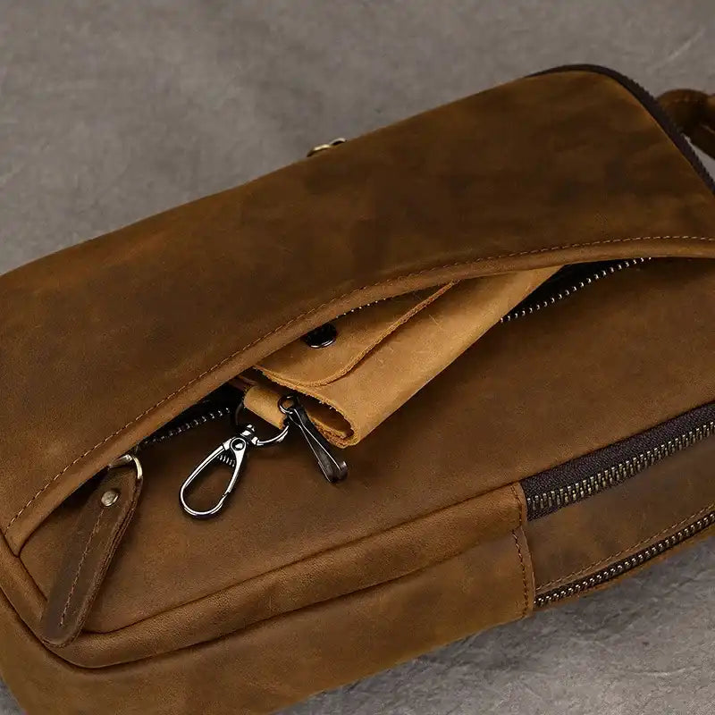 Brown leather crossbody bag with zipper details and front pocket.