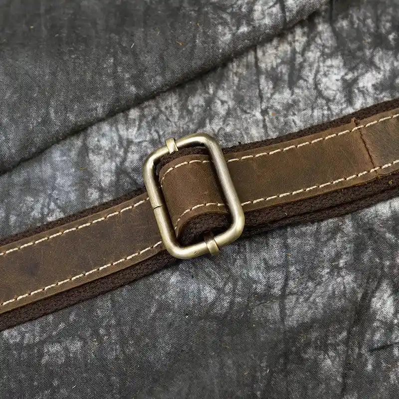 Close-up of a silver metal buckle on a brown leather strap on a textured background.