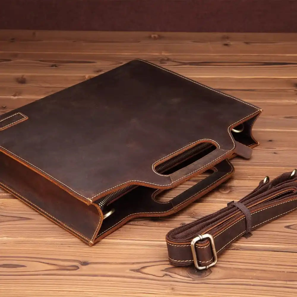 elegant brown leather briefcase with detachable strap on wooden surface.