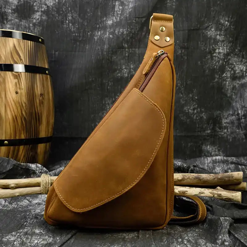 Brown leather sling bag featuring a zipper and front pocket - front view.