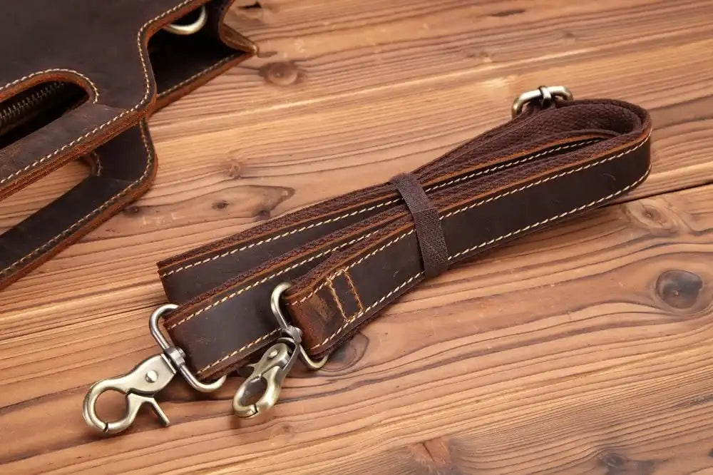 Brown leather detachable strap with metal clasps on a wooden surface.