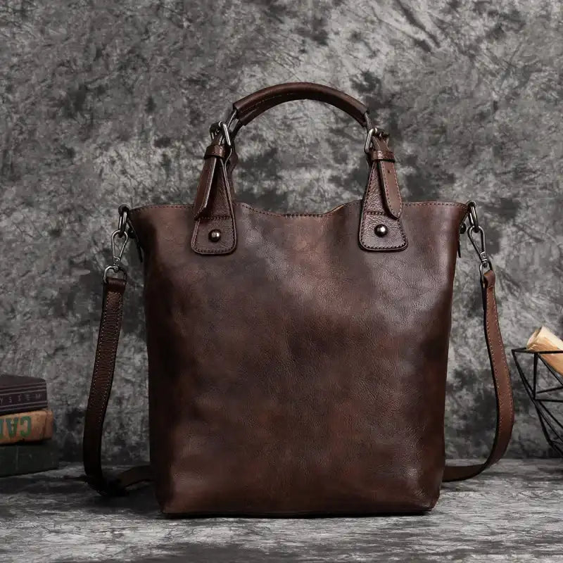 Brown leather handbag with handles, adjustable strap and metal details, front view.