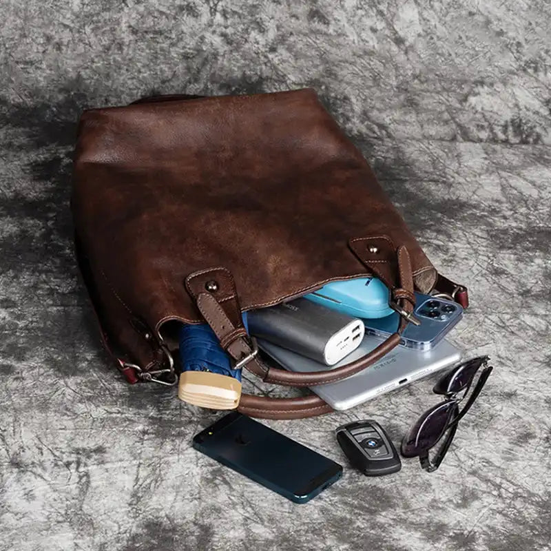 Open brown leather handbag, showing various items such as electronics and accessories.
