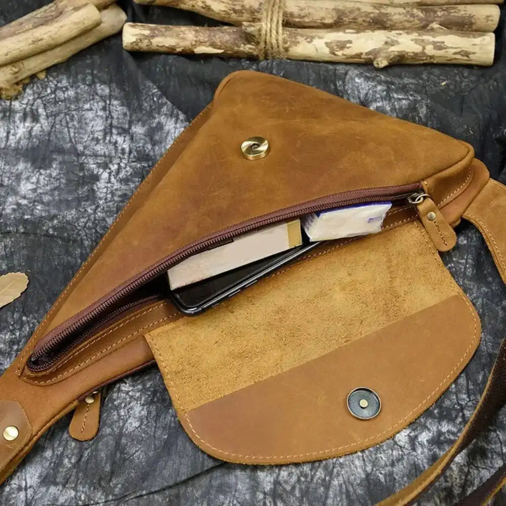 Open brown leather sling bag showcasing interior with phone and books.