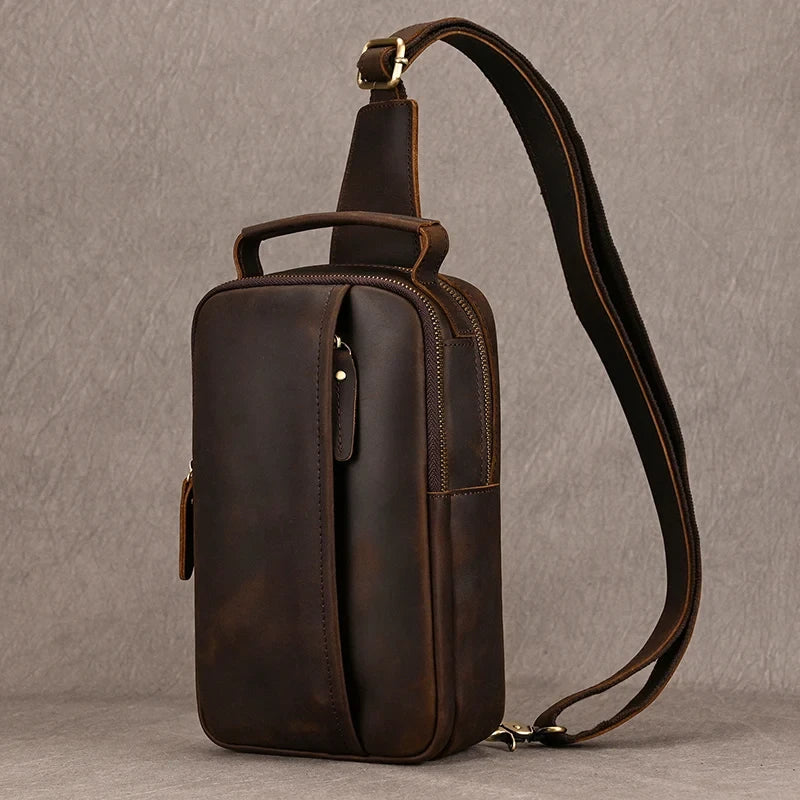 Dark brown leather crossbody bag with front zipped pocket, soft handle and adjustable strap, front view.