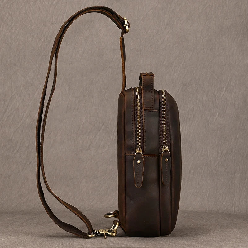 Dark brown leather crossbody bag with  zipped compartments, soft handle and adjustable strap, side view.