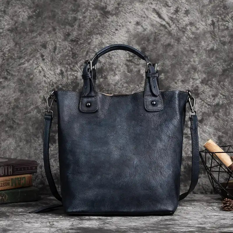 Gray leather handbag with handles, adjustable strap and metal details, front view.