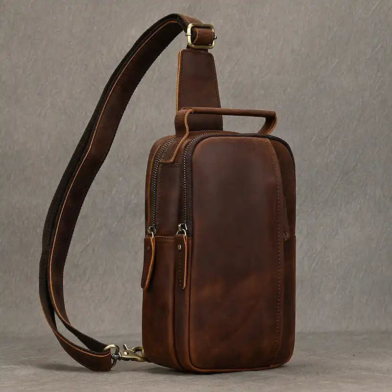 Red brown leather crossbody bag with front zipped pocket, soft handle and adjustable strap, front view.