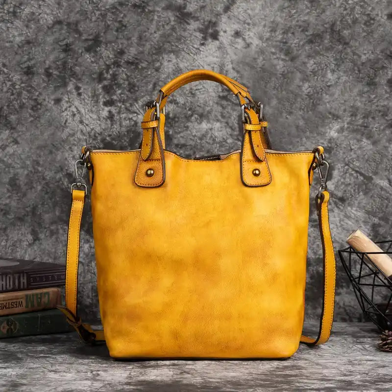 Yellow leather handbag with handles, adjustable strap and metal details, front view.