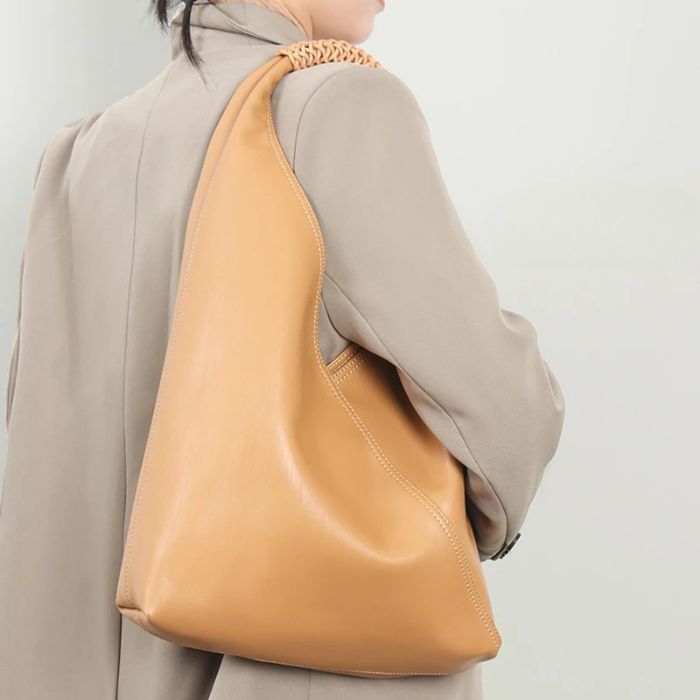 A modern gold leather bag with a braided strap, worn by a model on the shoulder.