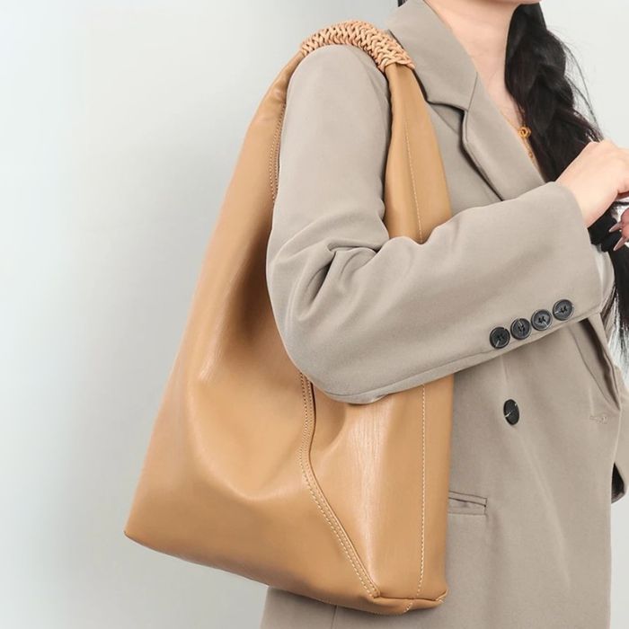 A gold color leather bag worn by a woman wearing a grey suit jacket.