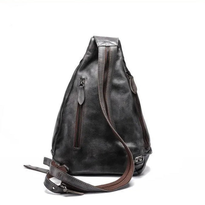 back view of a triangular shaped gray leather shoulder bag with multiple zippers and a unique strap design.