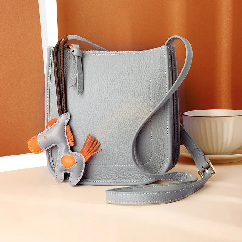 Front view of a fashionable crossbody in gray with a horse ornement for added charm.