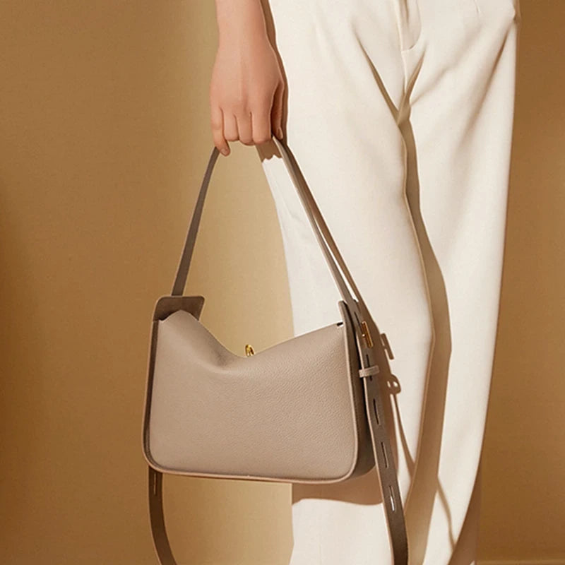 Elegant and modern gray leather bag with adjustable strap held by woman.
