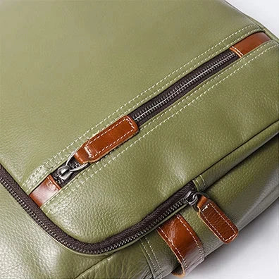Detail of a green leather bag with zippers and brown leather trim.
