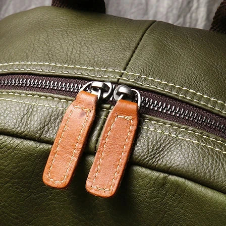 Zipper detail of a green leather backpack, with brown leather pulls that highlight the quality and style of the accessory.