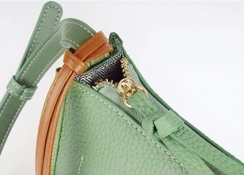 Close up of a trendy green crossbody bag showcasing its elegant zipper and strap.