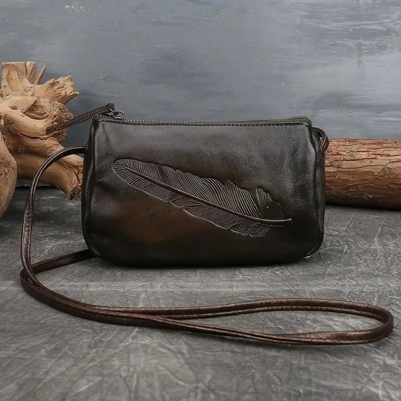 Dark green leather crossbody bag with colorful feather embossed detail, front view.