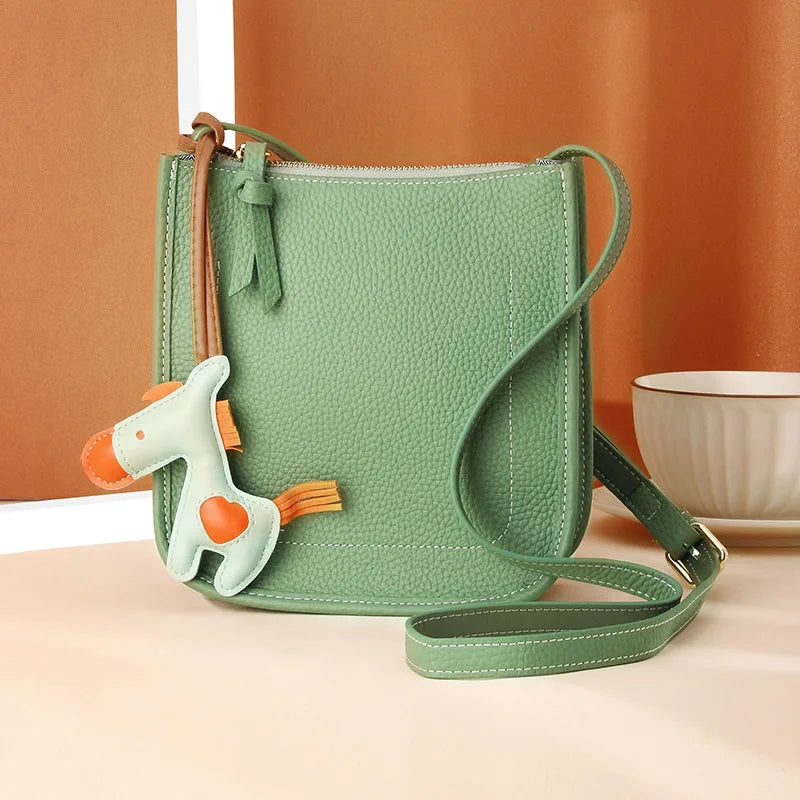 Front view of a trendy green crossbody bag with a playful horse accessory for a chic look.