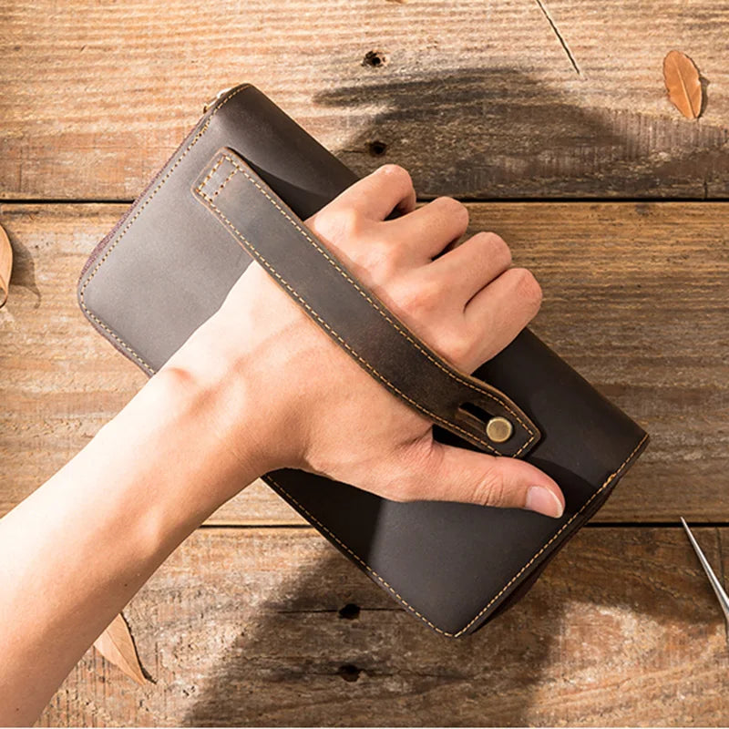 Close-up of a brown leather wallet being held by wrist strap showcasing its design.