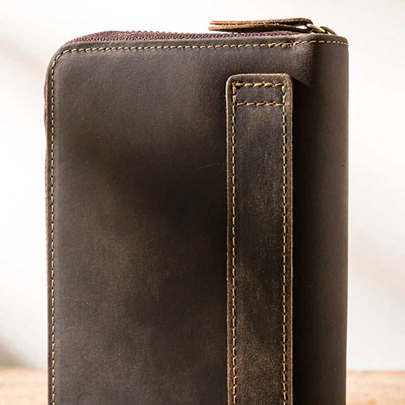 brown leather wallet featuring a zipper, a wrist strap and detailed stitching. 