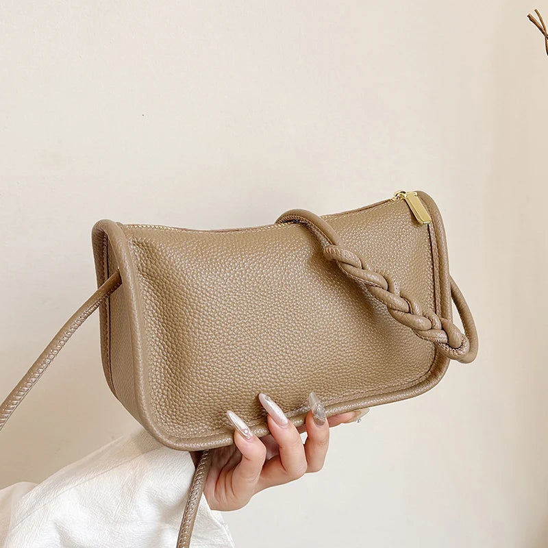 A fashionable khaki crossbody with braided strap held by a hand.