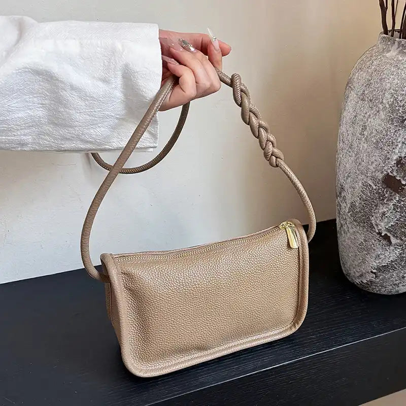 A stylish khaki crossbody bag with a braided strap held by a person.