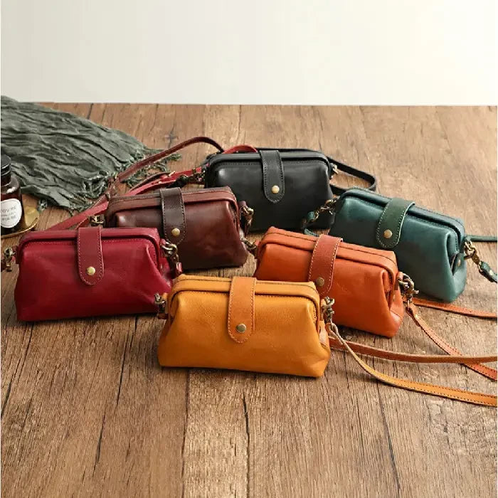 Set of leather bags in different colors, including red, brown, green and orange, on a wooden surface, front view.