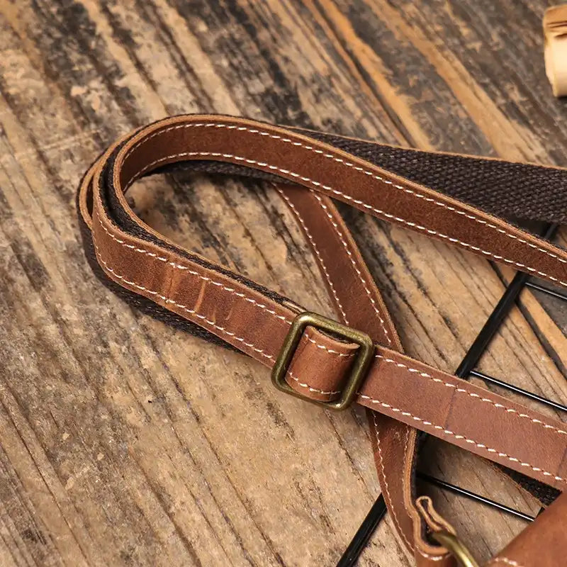Close-up of a brown leather bag strap featuring a metal buckle and buckle.