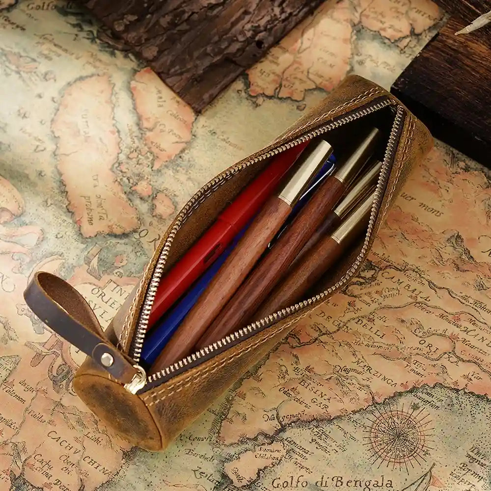 An open zippered brown leather pen case showcasing various pens on an antique map.