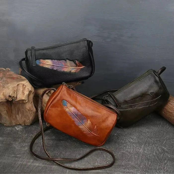 Display of three leather crossbody bags with colorful feather prints, highlighting style and elegance, front view.