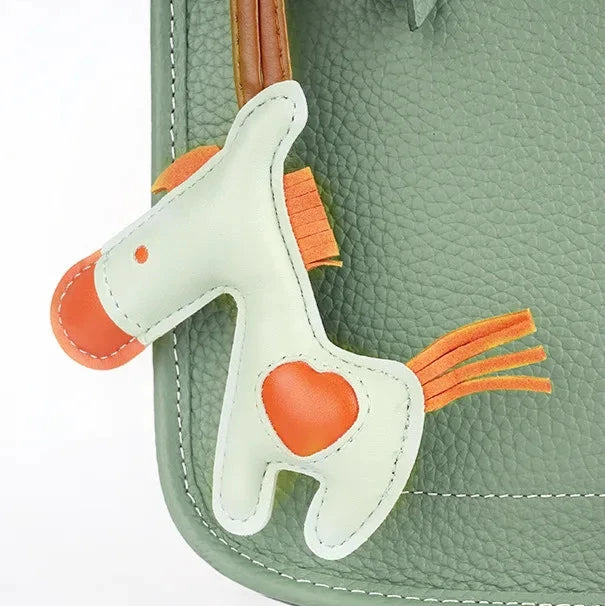 Close-up on cute leather horse charm accessory on a stylish green crossbody bag
