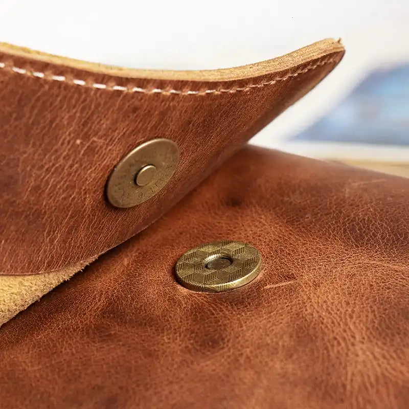 Close-up of a brown leather bag showcasing brass snap button.