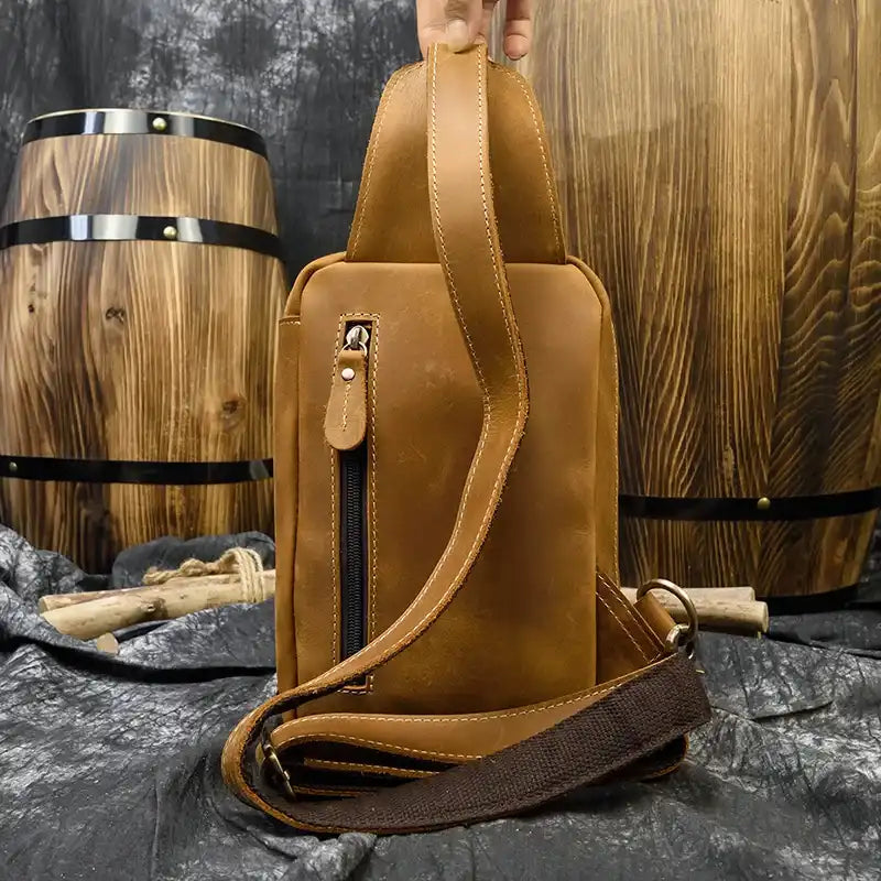 Brown leather bag with a classic design and a long strap and back zipped pocket, back view.