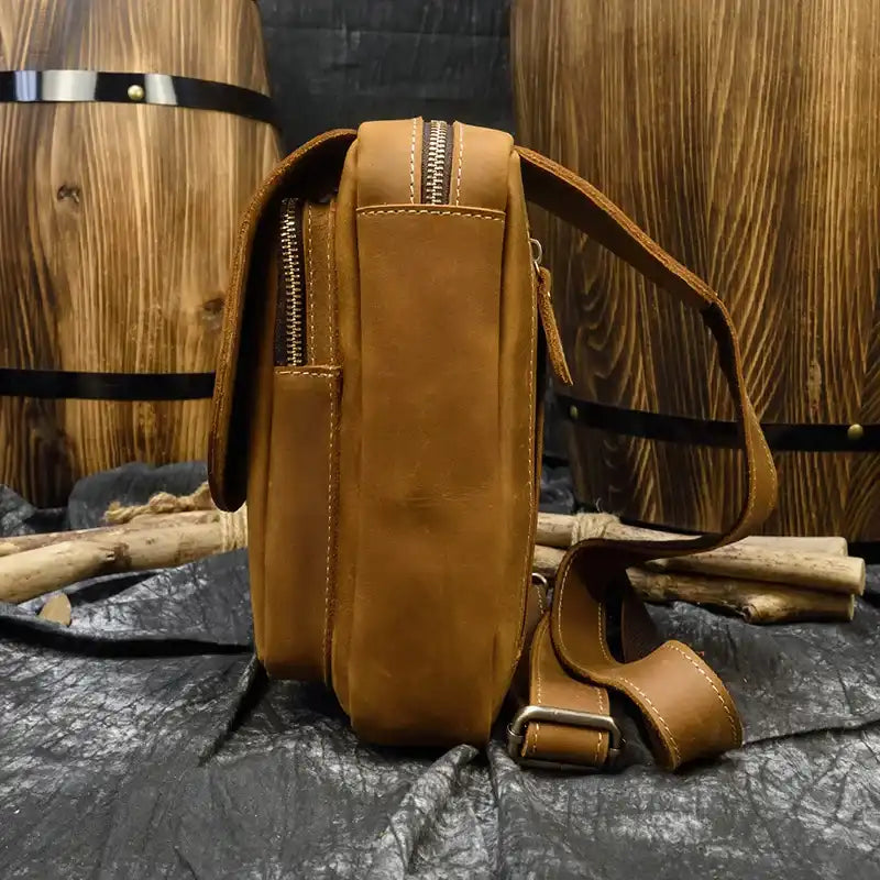 a brown leather bag with a modern design, highlighting zipper and adjustable strap details, side view.