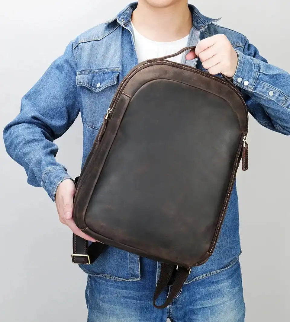 A man holding a brown leather backpack showcasing a modern and stylish design, front view.