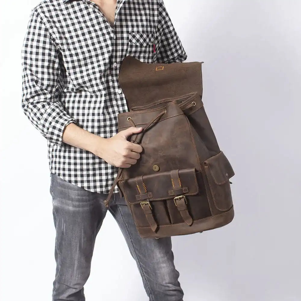 Man wearing holding a brown leather backpack, with several compartments,  ideal for travel and everyday use.