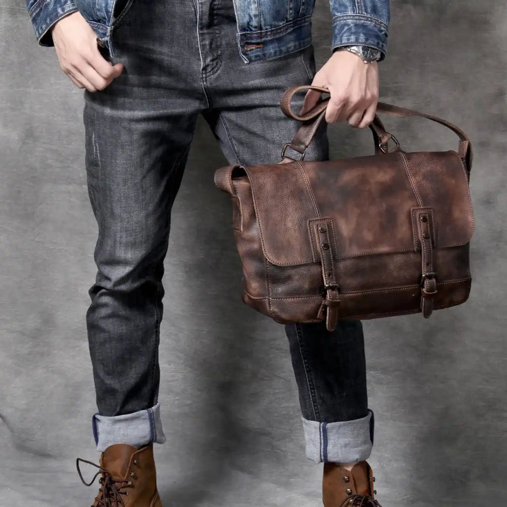 man wearing dark jeans and brown boots, holding a brown leather bag with style.