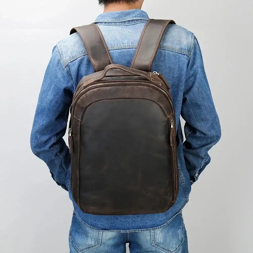 Back view of a man wearing a denim jacket, carrying a brown leather backpack, highlighting elegance and functionality.