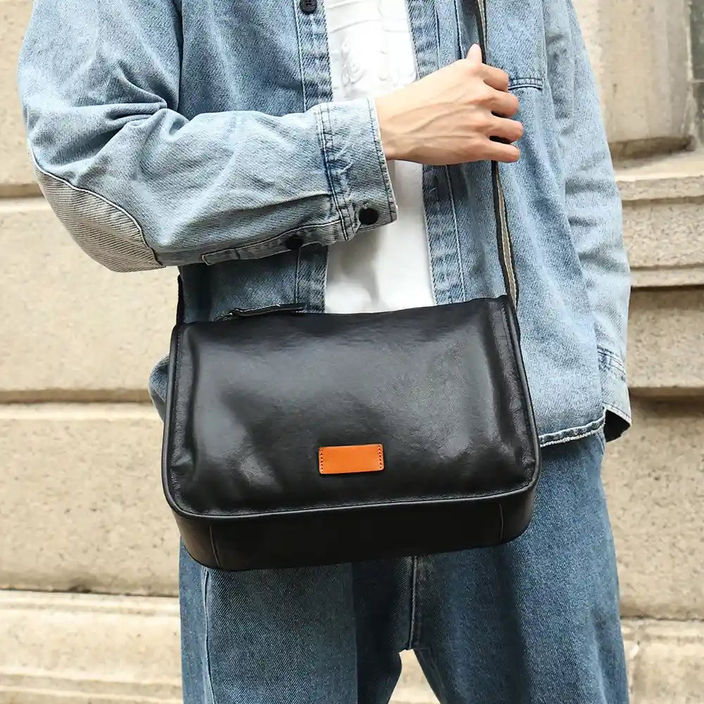 man carrying a black leather shoulder bag wearing a denim jacket. The bag is modern and practical.