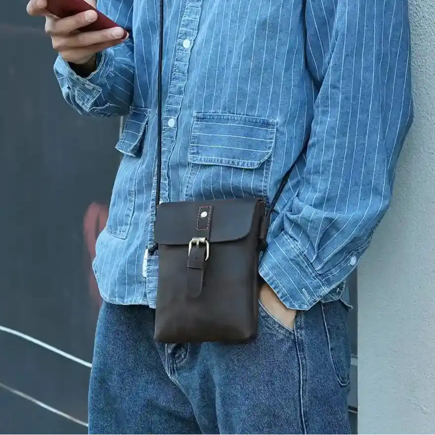 a person wearing a blue denim shirt and carrying a brown leather crossbody bag.