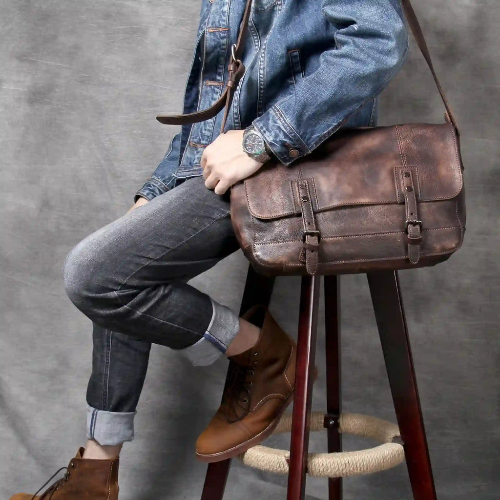 a person sitting on a stool, wearing a denim jacket and holding a brown leather shoulder bag.