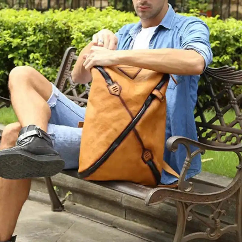 Man sitting with a stylish brown vintage  leather backpack with unique design, on park bench.