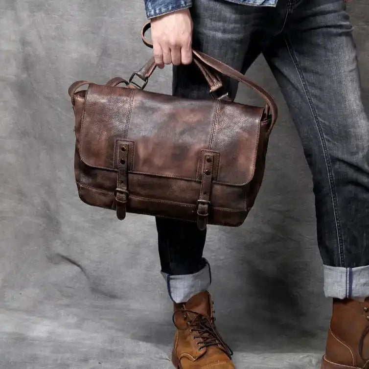 A man holding a brown leather bag, wearing a denim shirt and dark pants,  in a casual pose.
